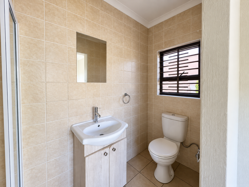 A clean and functional bathroom featuring a vanity cabinet with a basin, a toilet, and neutral wall tiling.