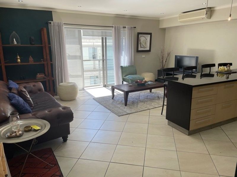 Spacious open-plan living area featuring tiled floors, a modern kitchen island, and direct access to a balcony through sliding glass doors.
