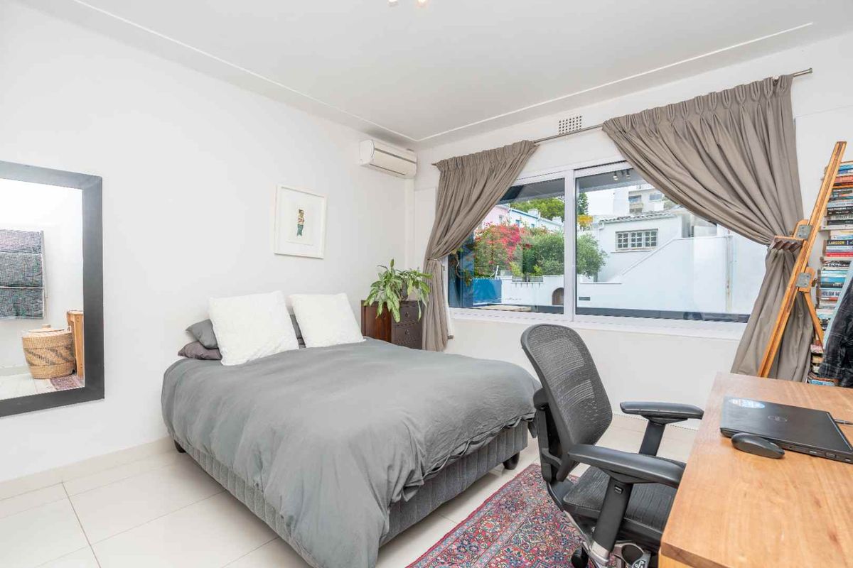 A bright bedroom featuring tiled flooring, a wall-mounted air conditioning unit, and a large window providing natural light and an exterior view.