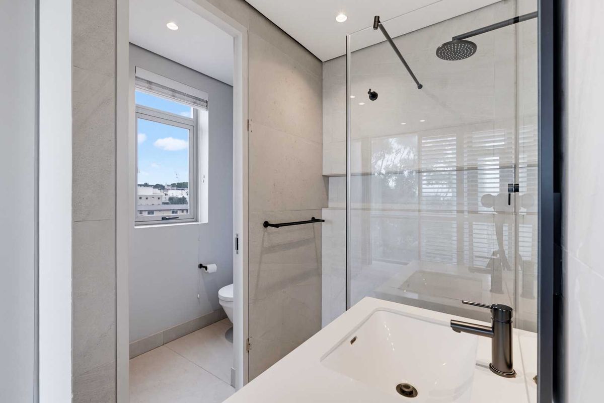 Modern bathroom featuring a walk-in shower with a rain shower head, black matte fixtures, and a clean, contemporary tiled finish.