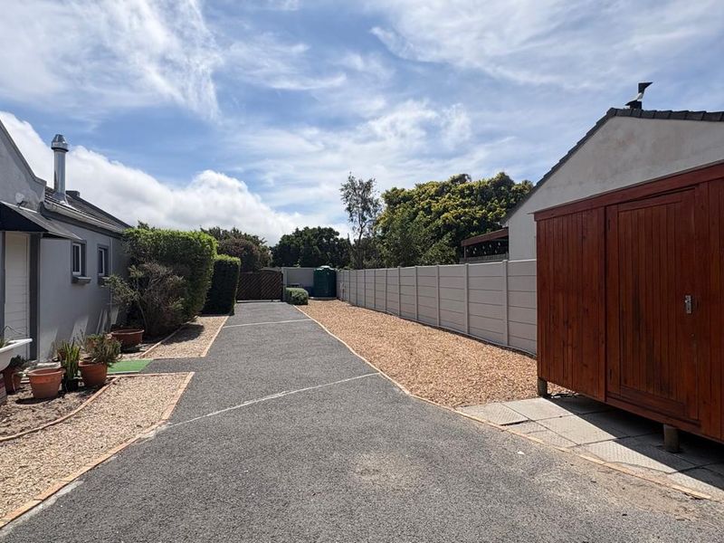 A well-maintained rear exterior area featuring an asphalt driveway, gravel landscaping, and a secure precast concrete boundary wall with a wooden storage shed.
