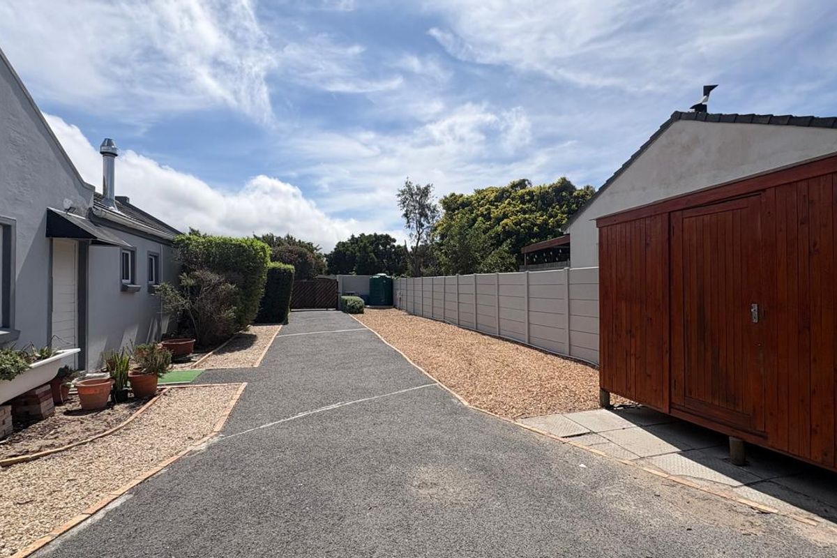 A well-maintained rear exterior area featuring an asphalt driveway, gravel landscaping, and a secure precast concrete boundary wall with a wooden storage shed.