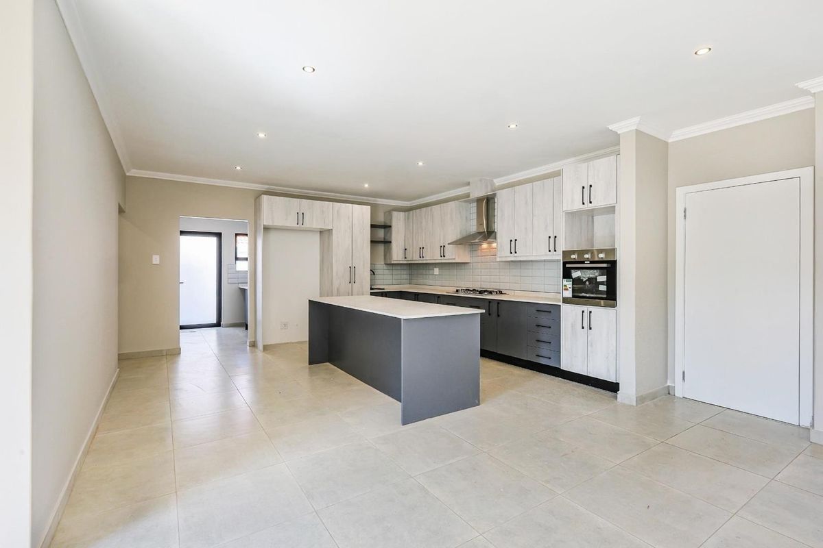 Modern open-plan kitchen featuring a central island, built-in oven, gas hob, extractor fan, and neutral tiled flooring with ample cabinetry.