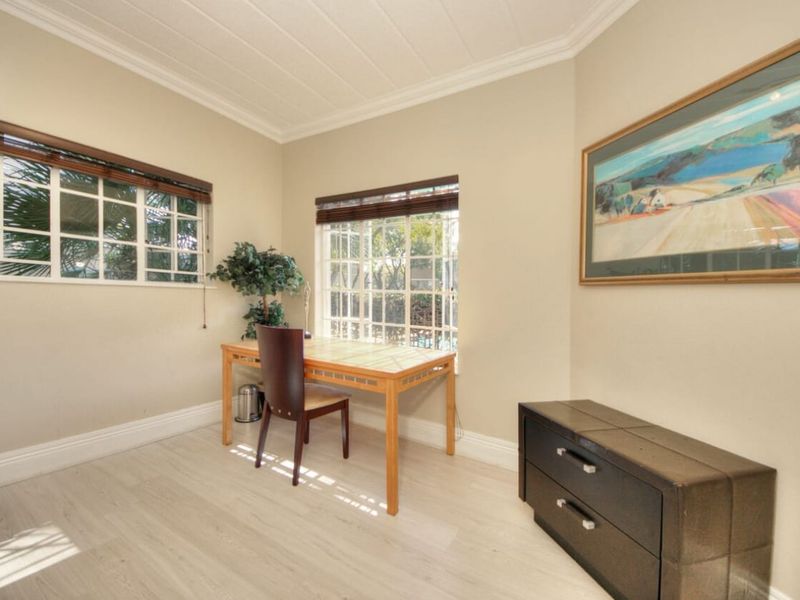 A bright and functional office space featuring light-toned laminate flooring, crown molding, and large lattice windows that provide ample natural light.