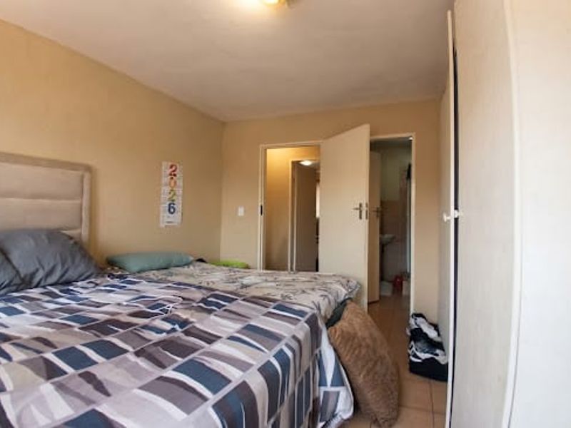 A bedroom featuring built-in wardrobes and tiled flooring, with an adjacent doorway leading to a bathroom area.