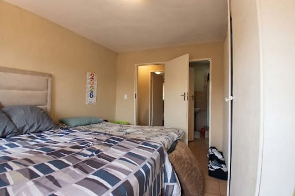 A bedroom featuring built-in wardrobes and tiled flooring, with an adjacent doorway leading to a bathroom area.