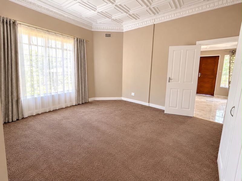 A spacious, empty bedroom featuring a decorative coffered ceiling, ornate cornice, neutral wall tones, and plush carpeting, offering a clean canvas for personalization.