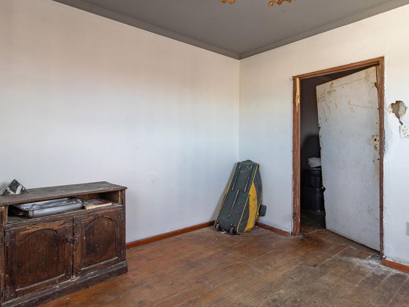 A vacant bedroom featuring original timber flooring and a doorway requiring repair to the surrounding wall and frame.