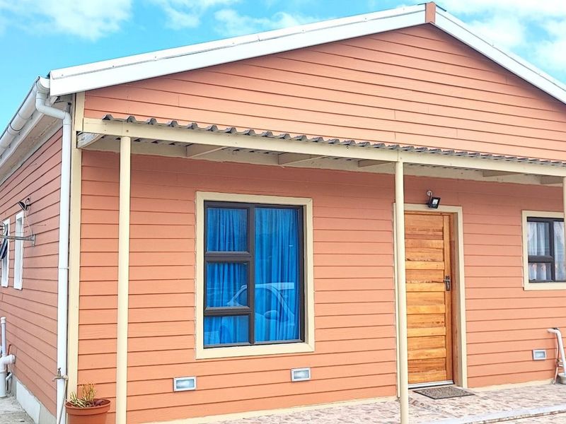 Front elevation of a timber-clad house featuring a covered patio, timber entrance door, and aluminium window frames.
