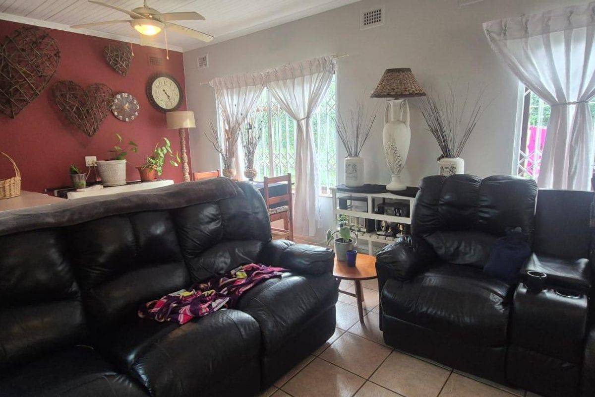 A comfortable living room featuring tiled flooring, a ceiling fan, and a timber-look ceiling, with large windows fitted with security gates.