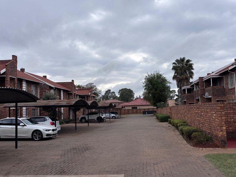 Exterior view of an apartment complex featuring brick buildings, a paved driveway, and covered carport parking spaces.