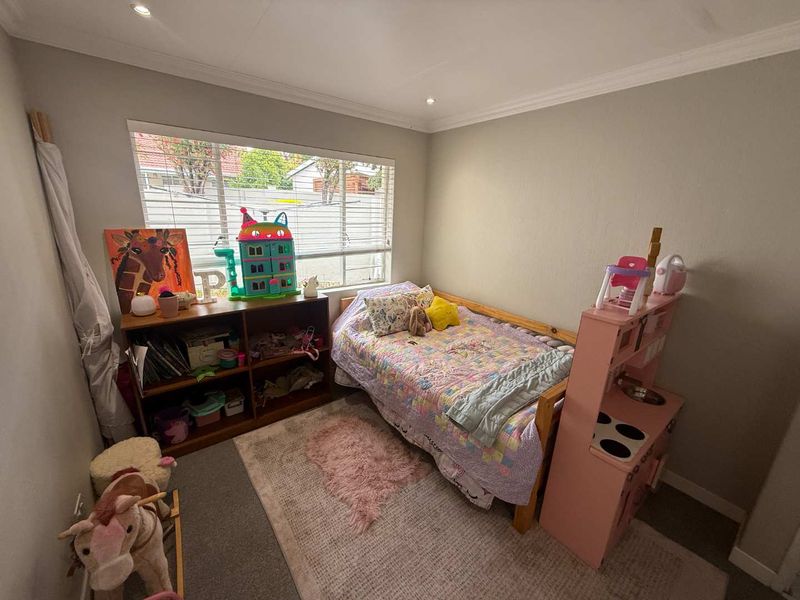 A functional bedroom featuring neutral wall finishes, recessed downlighting, and a large window with venetian blinds, providing ample natural light.