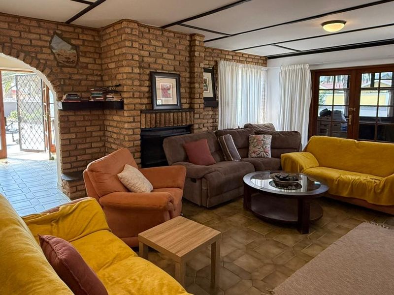 Spacious living room featuring an exposed brick fireplace, tiled flooring, and exposed beam ceiling with direct access to the outdoor area through french doors.