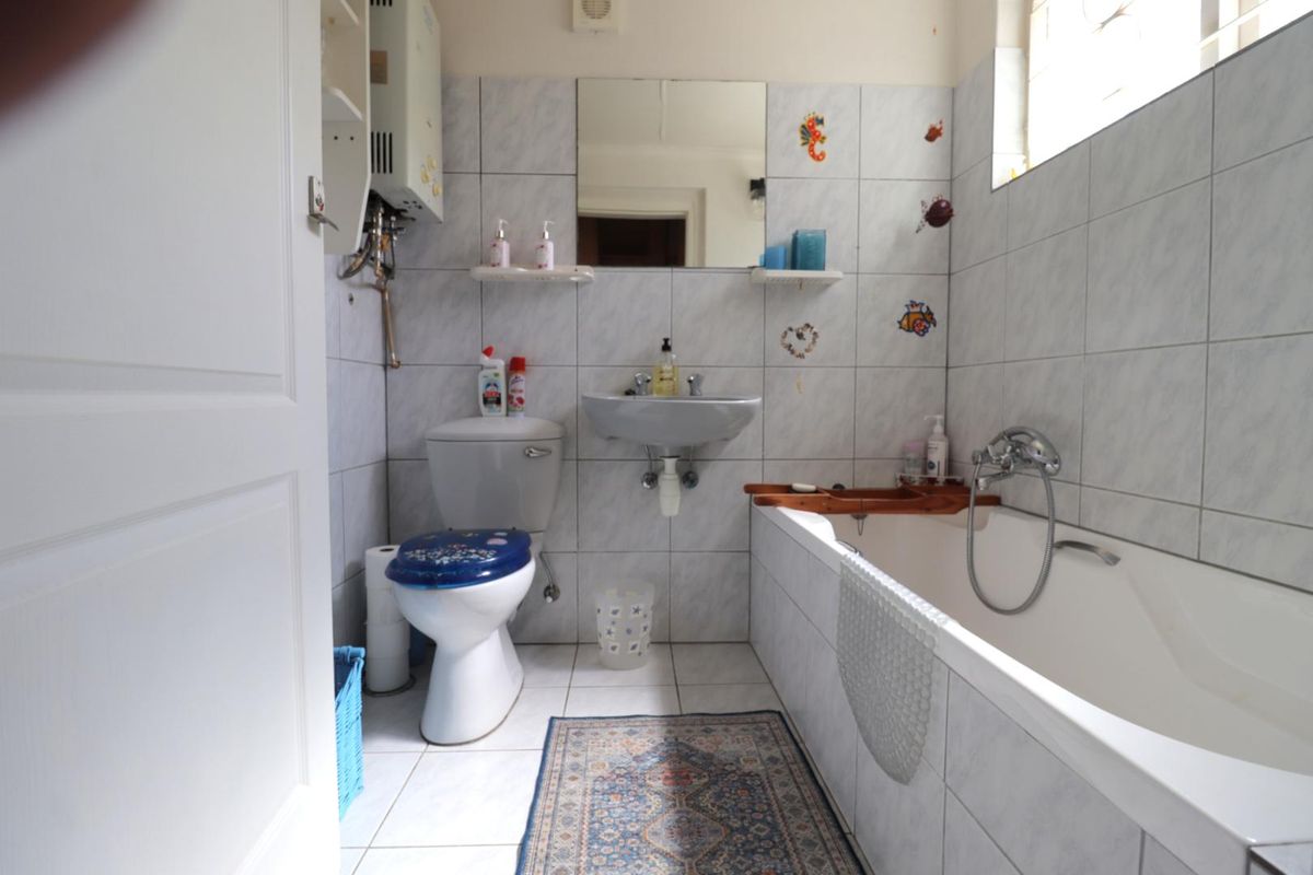 A functional bathroom featuring a bathtub with handheld shower mixer, wall-mounted basin, toilet, and a wall-mounted gas geyser unit.