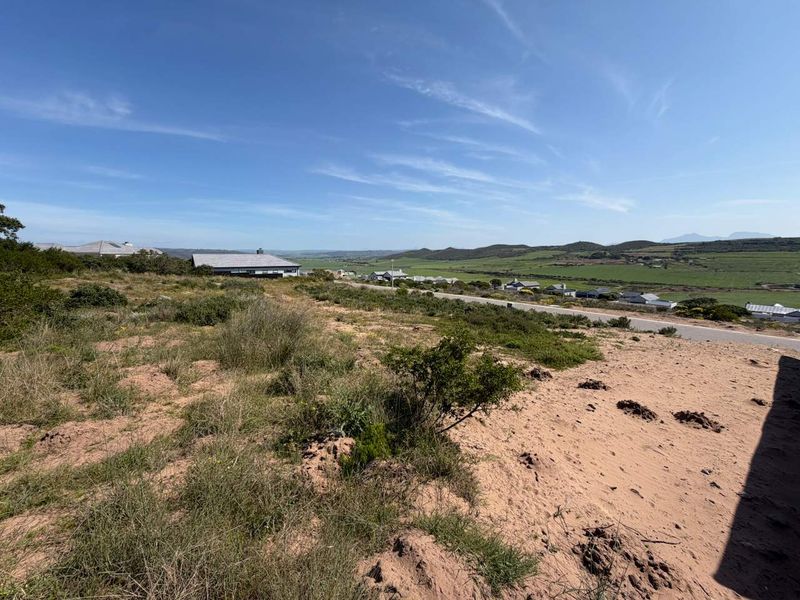 A wide-angle view of the vacant residential land, showcasing the natural landscape, surrounding terrain, and nearby neighborhood infrastructure.