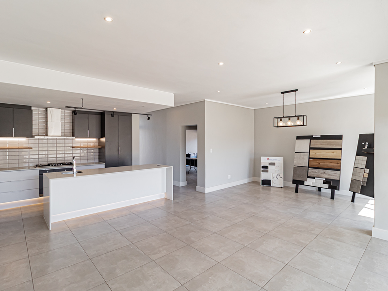 Modern open-plan kitchen featuring a central island, sleek cabinetry, subway tile backsplash, and neutral tiled flooring in a bright, spacious living area.