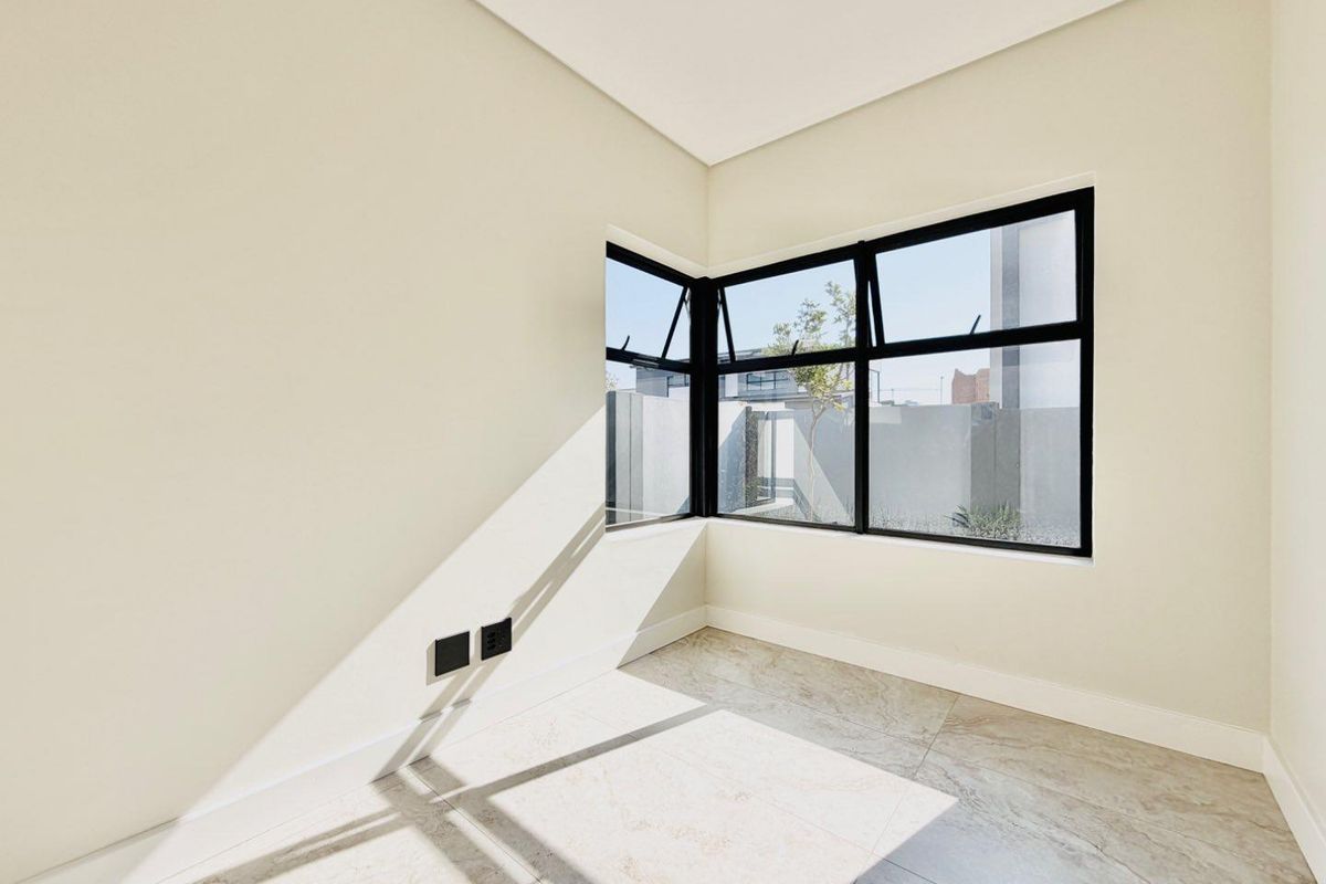 A bright, modern, and empty bedroom featuring large corner windows with black aluminium frames and neutral tiled flooring.