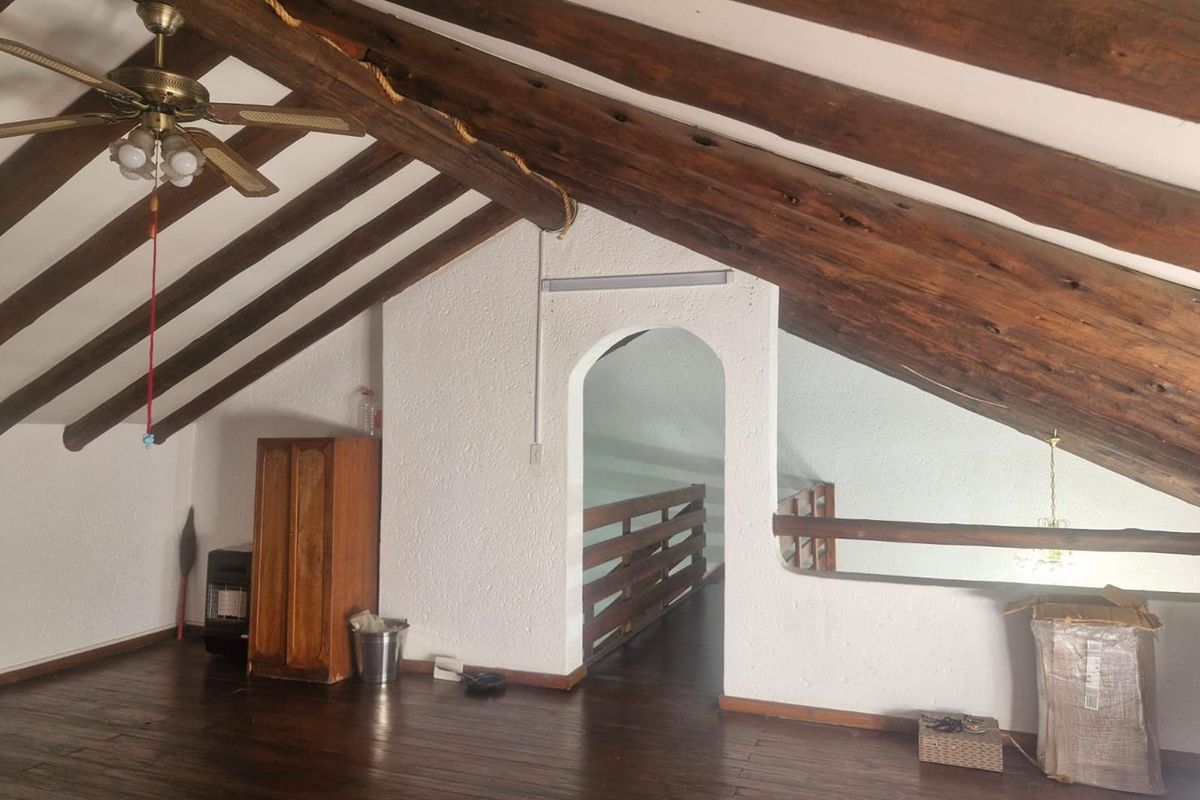 An attic-style bedroom featuring exposed timber ceiling beams, a vaulted ceiling, and dark wood flooring, accessible via an arched doorway.