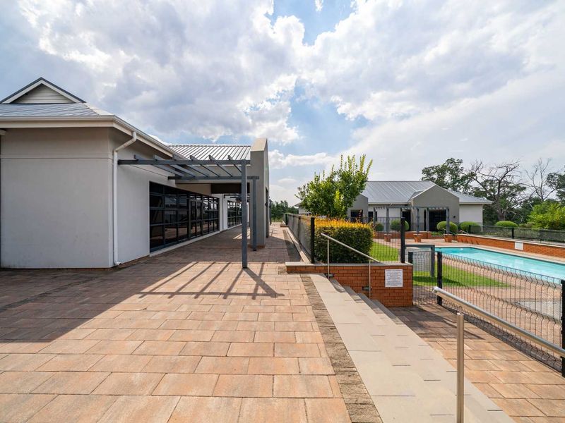 A well-maintained outdoor pool area featuring a paved patio, pergola structure, and secure metal fencing, providing a clean and functional communal space.