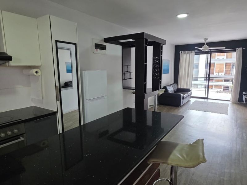 Open-plan living area featuring a modern kitchen with black granite countertops, built-in appliances, and direct access to a balcony through sliding glass doors.