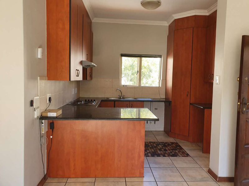 A functional kitchen featuring wooden cabinetry, granite countertops, a built-in hob with extractor, and tiled flooring, offering a clean and practical workspace.