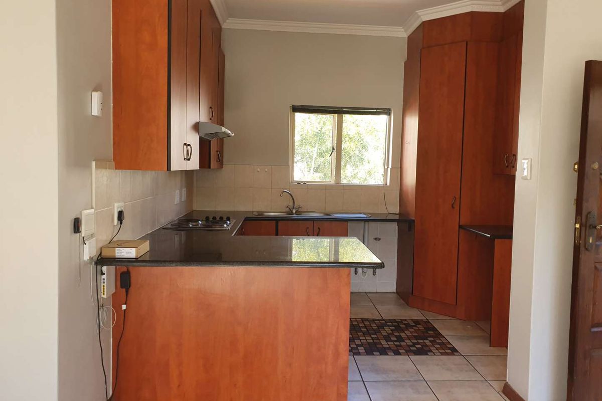 A functional kitchen featuring wooden cabinetry, granite countertops, a built-in hob with extractor, and tiled flooring, offering a clean and practical workspace.