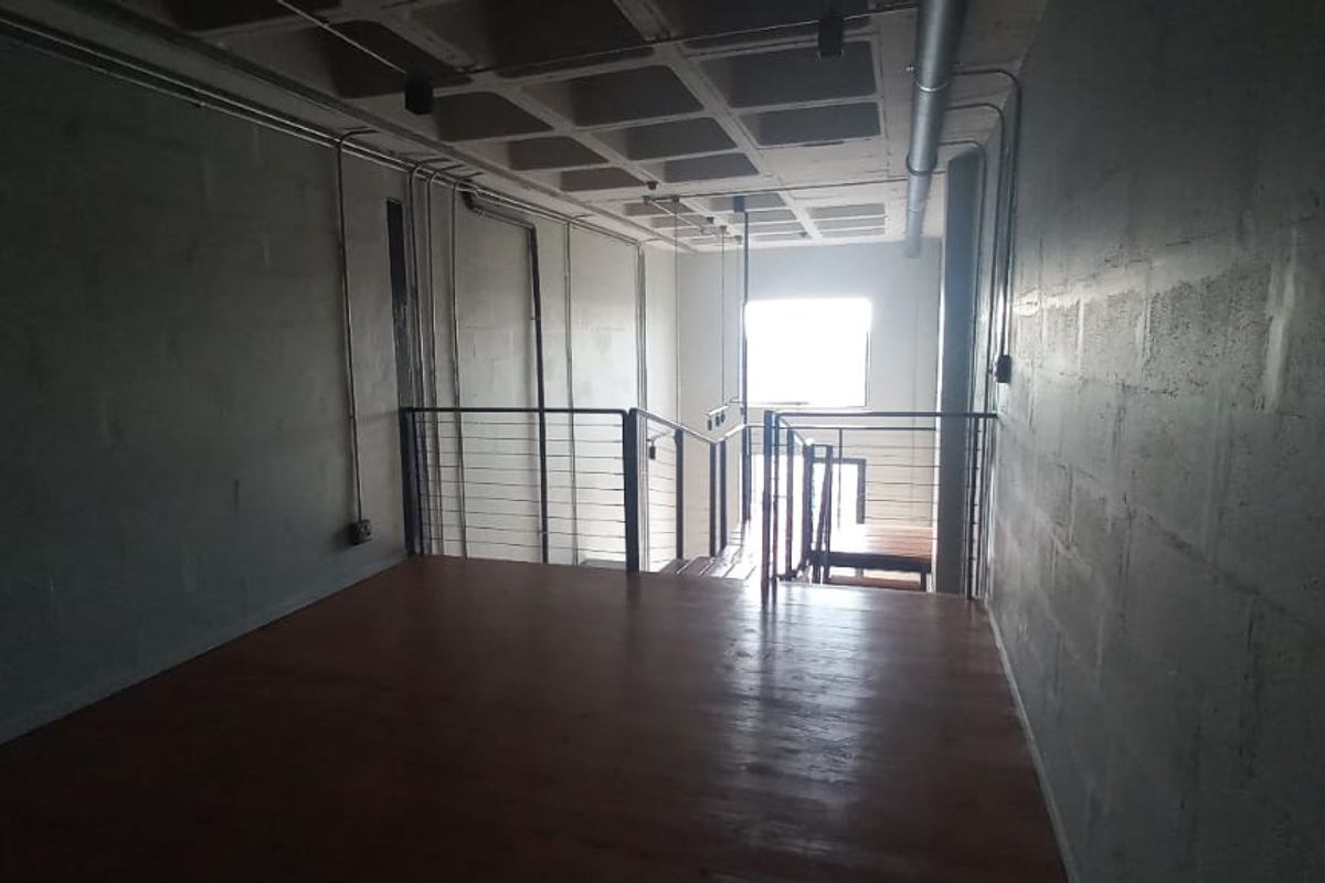 An industrial-style loft space featuring exposed concrete waffle ceilings, timber flooring, and metal balustrades, overlooking a staircase area.