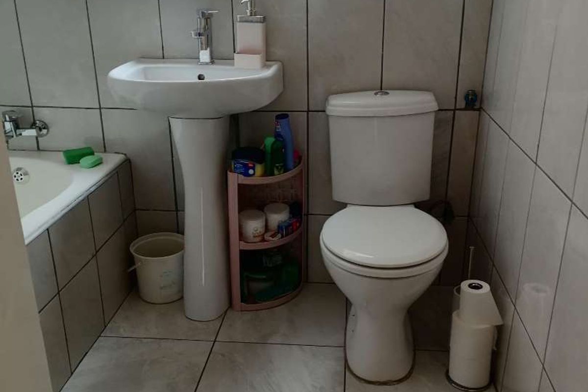 A functional bathroom featuring a pedestal basin, a standard toilet, and a tiled bathtub with wall-mounted fixtures.