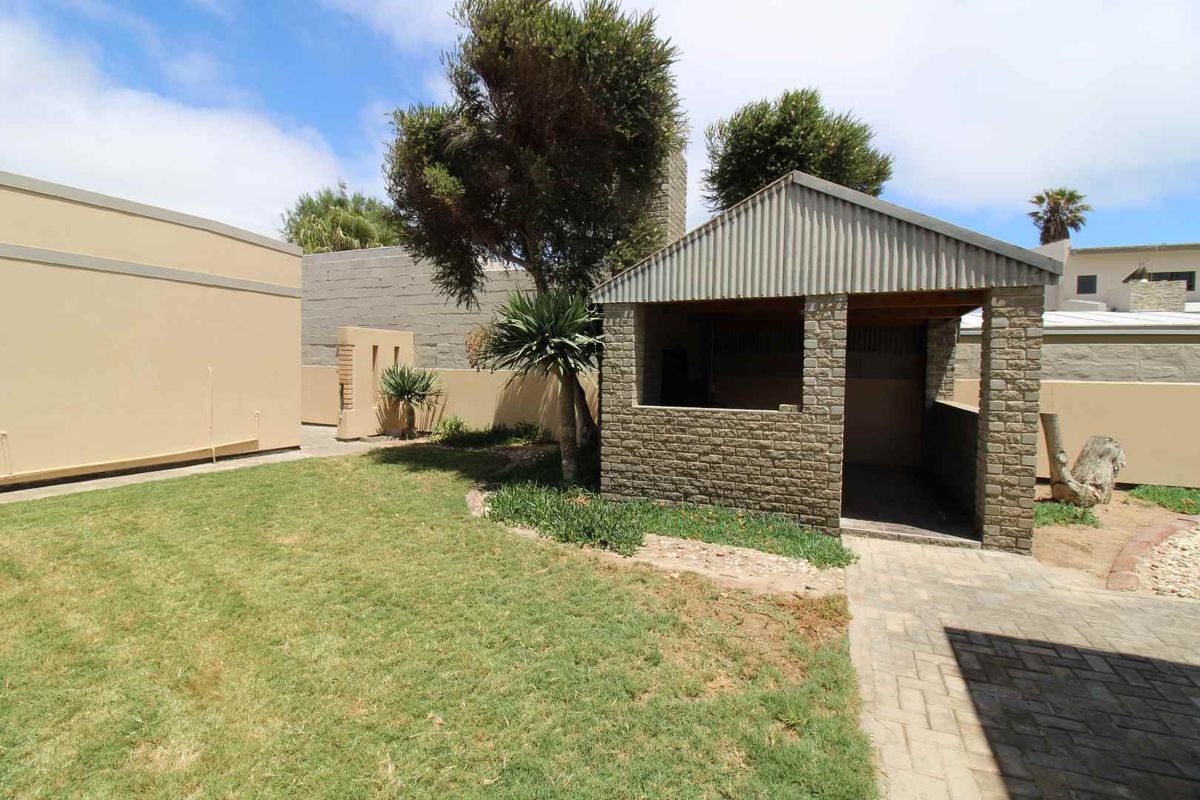 A rear garden area featuring a covered brick and corrugated iron outdoor entertainment structure, paved walkway, and surrounding boundary walls.