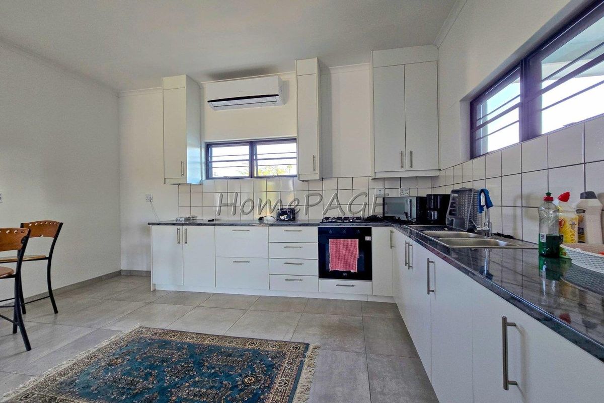 A functional kitchen featuring white cabinetry, dark granite countertops, tiled splashbacks, a built-in oven, and a wall-mounted air conditioning unit.