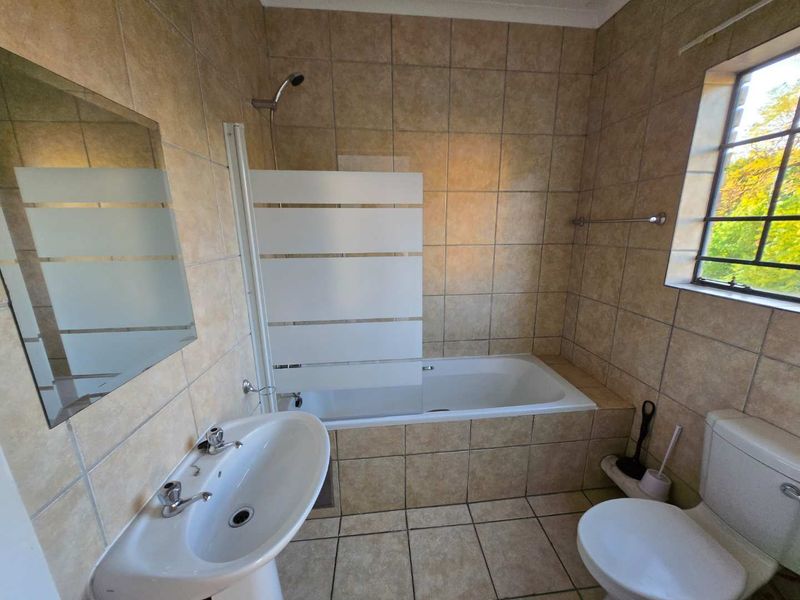 A functional bathroom featuring a pedestal basin, bathtub with a shower screen, and tiled finishes throughout.