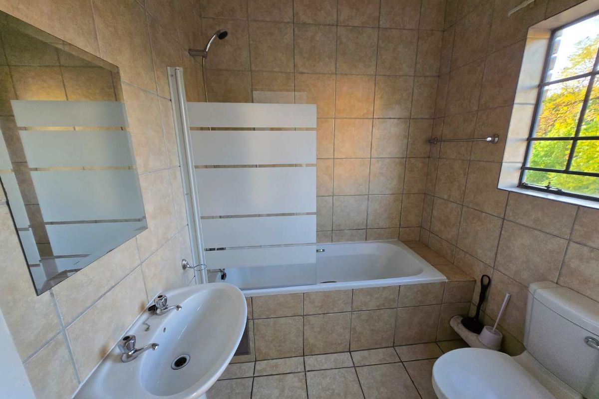 A functional bathroom featuring a pedestal basin, bathtub with a shower screen, and tiled finishes throughout.