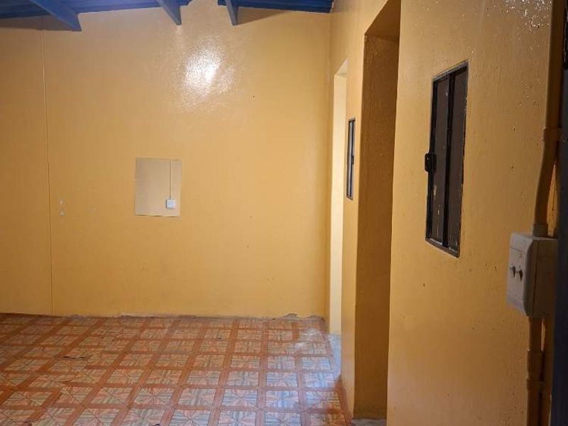 An empty utility space featuring exposed beam ceilings and tiled flooring, currently showing signs of wear and damage to the floor tiles.
