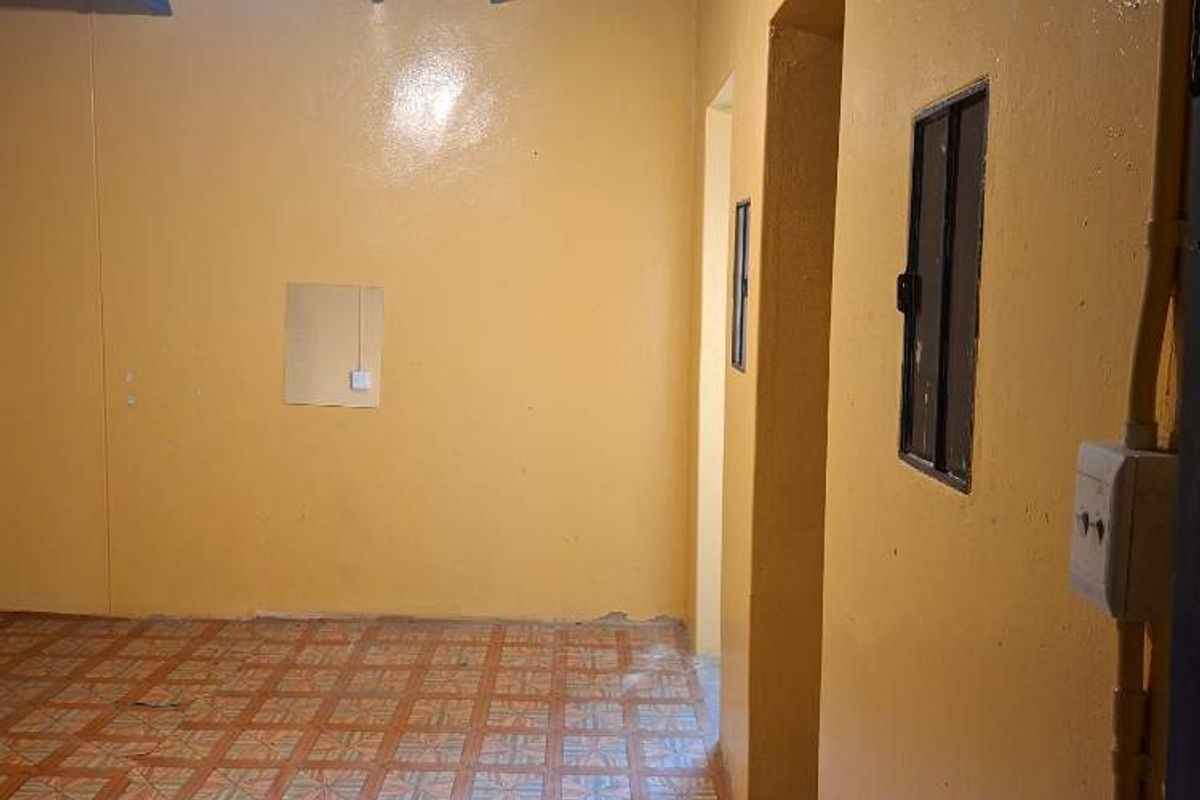 An empty utility space featuring exposed beam ceilings and tiled flooring, currently showing signs of wear and damage to the floor tiles.