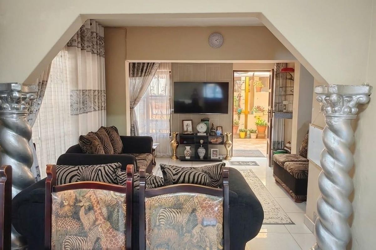 A living room area featuring decorative columns and an archway leading to an adjacent space with tiled flooring throughout.