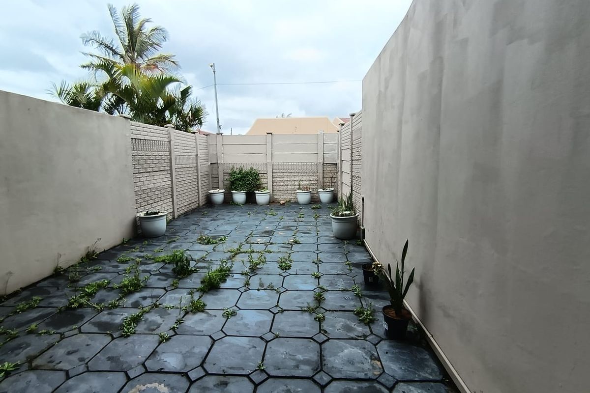 A private rear courtyard featuring paved flooring and high precast concrete boundary walls, currently requiring maintenance to clear weeds.