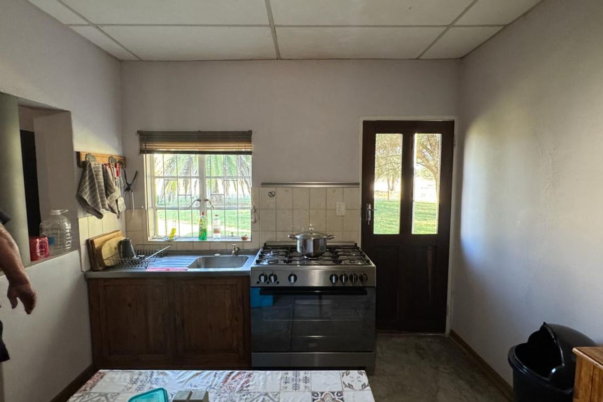 A functional kitchen featuring a stainless steel gas stove, built-in sink, wooden cabinetry, and direct access to the exterior through a timber door.