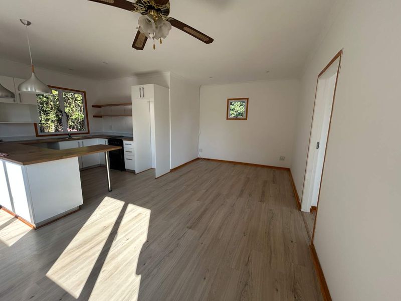 Bright open-plan living and kitchen area featuring modern laminate flooring, wooden countertops, and clean white cabinetry in a cottage-style layout.