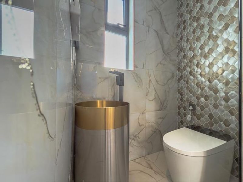A modern bathroom featuring a sleek pedestal washbasin, wall-mounted toilet, and a combination of marble-look and hexagonal mosaic wall tiling.