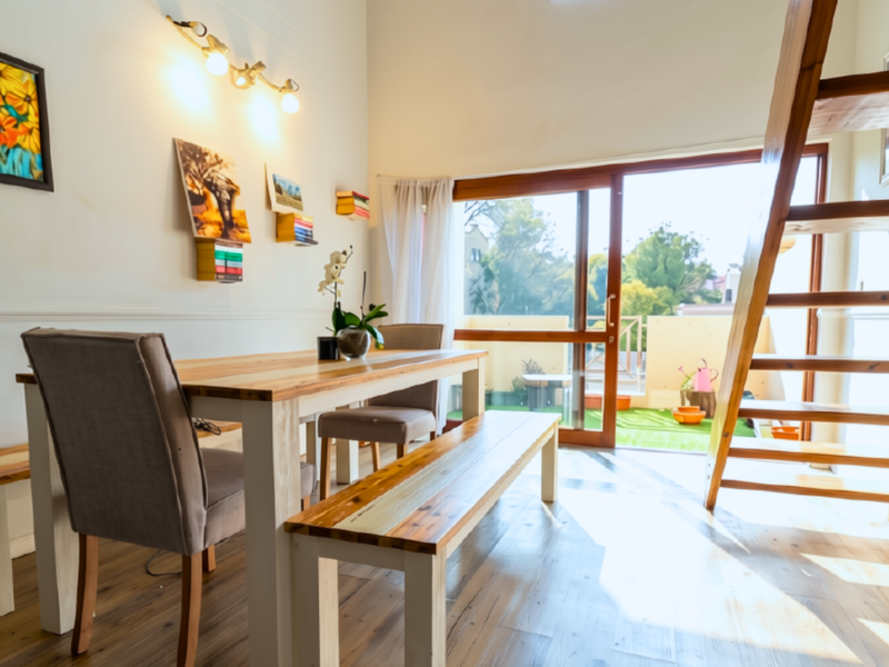 Bright open-plan living area featuring laminate flooring, wainscoting, a wooden staircase, and large sliding glass doors leading to an outdoor balcony.