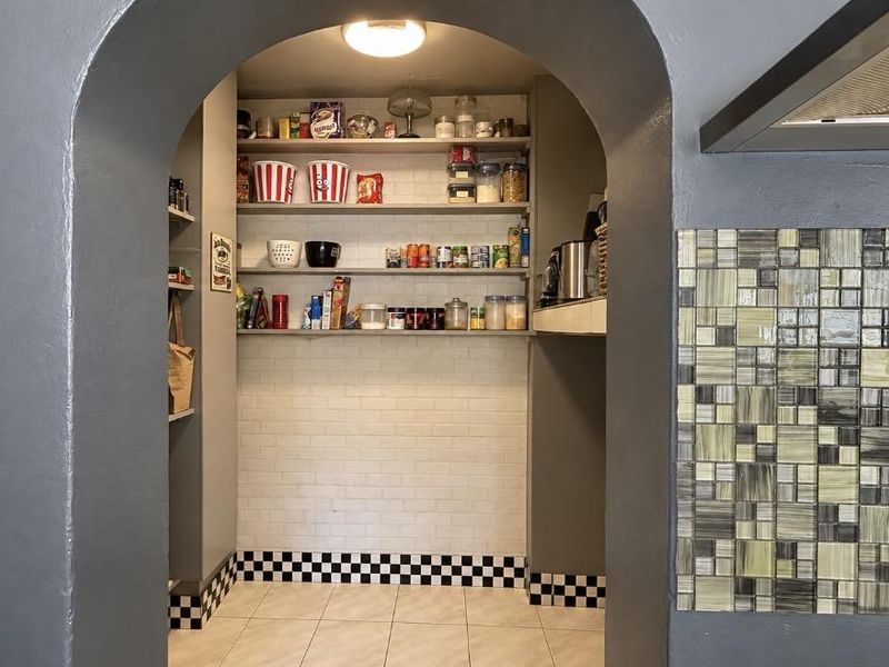 A functional scullery or pantry area featuring built-in shelving, tiled flooring, and a decorative mosaic tiled wall section.