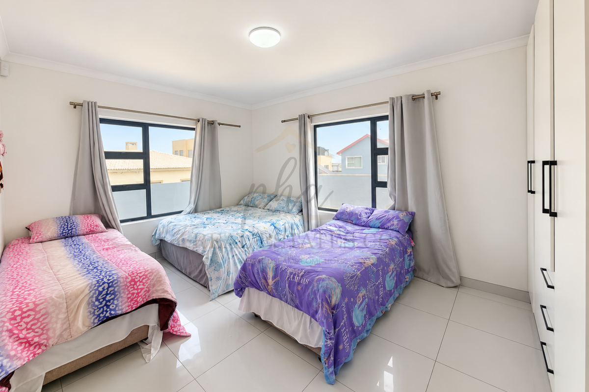 Spacious bedroom featuring large windows, neutral tiled flooring, and extensive built-in cupboard storage.