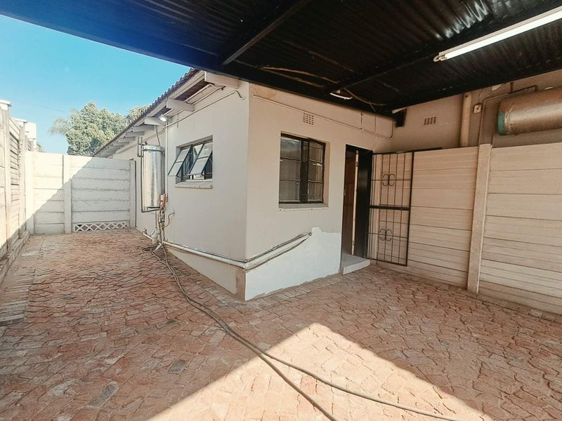 Rear exterior view showing a covered patio area with paved flooring, precast boundary walls, and an external solar geyser installation.