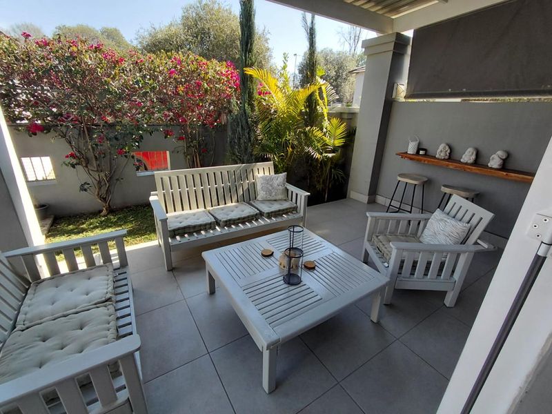 A covered outdoor patio featuring tiled flooring, a built-in shelf, and direct access to a landscaped garden area.