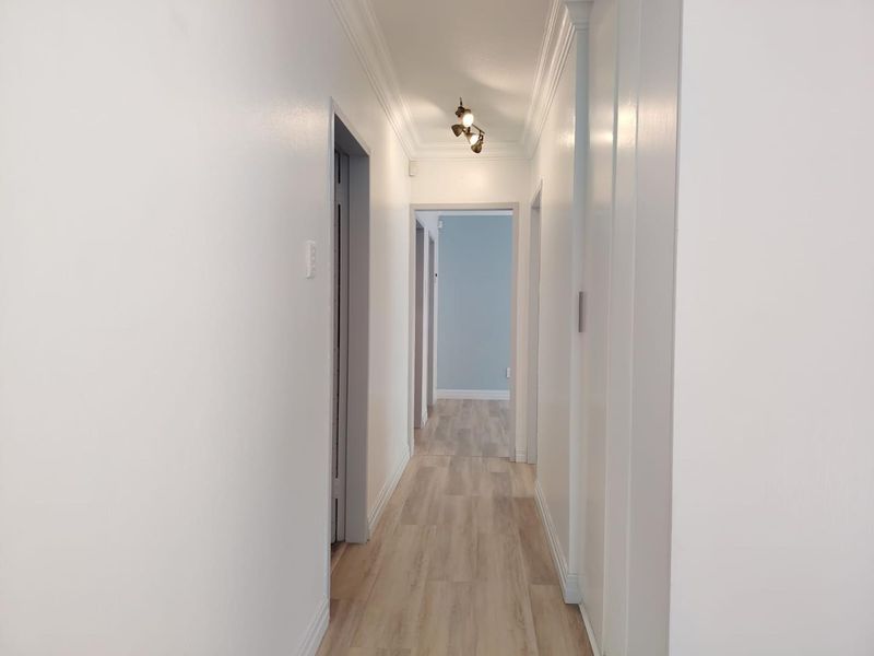 A clean, well-maintained hallway featuring light wood-look laminate flooring, crown molding, and a built-in storage cupboard.
