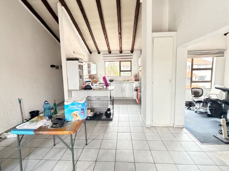 Open plan living and kitchen area featuring high vaulted ceilings with exposed timber beams and tiled flooring throughout.