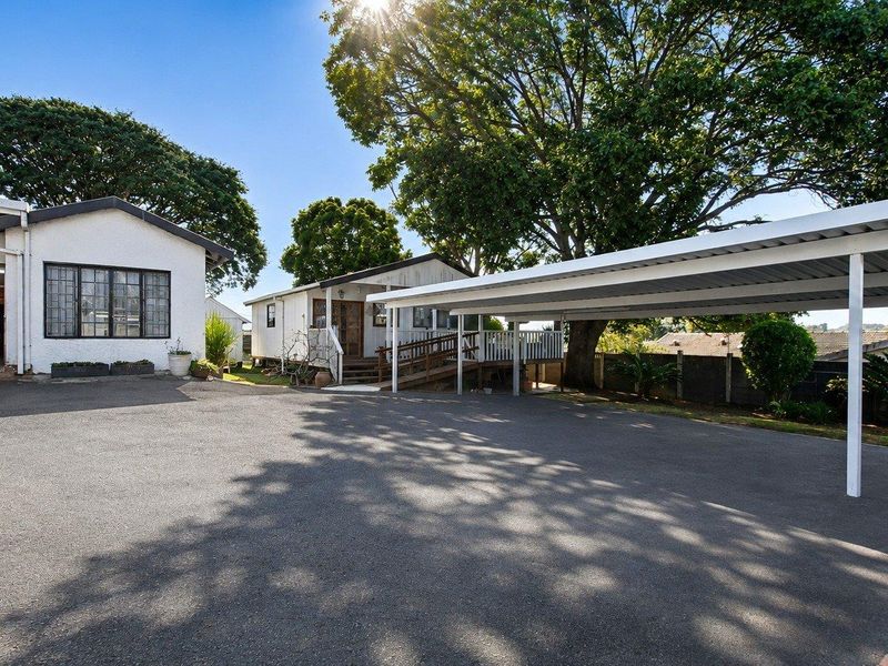 Front exterior view featuring a spacious asphalt driveway, a large metal carport, and a timber entrance ramp leading to the main dwelling.