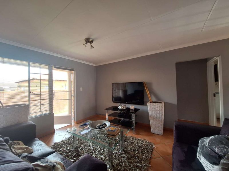 A living room featuring tiled flooring, neutral grey walls, and a glass door leading to an outdoor area with security gate.