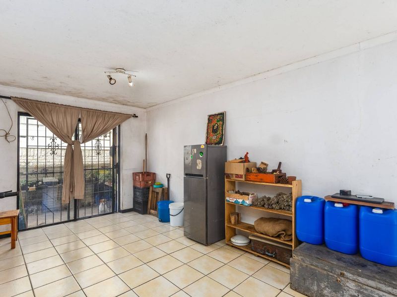 A living area featuring tiled flooring and a sliding glass door with security gate, showing signs of ceiling water damage and wall wear.