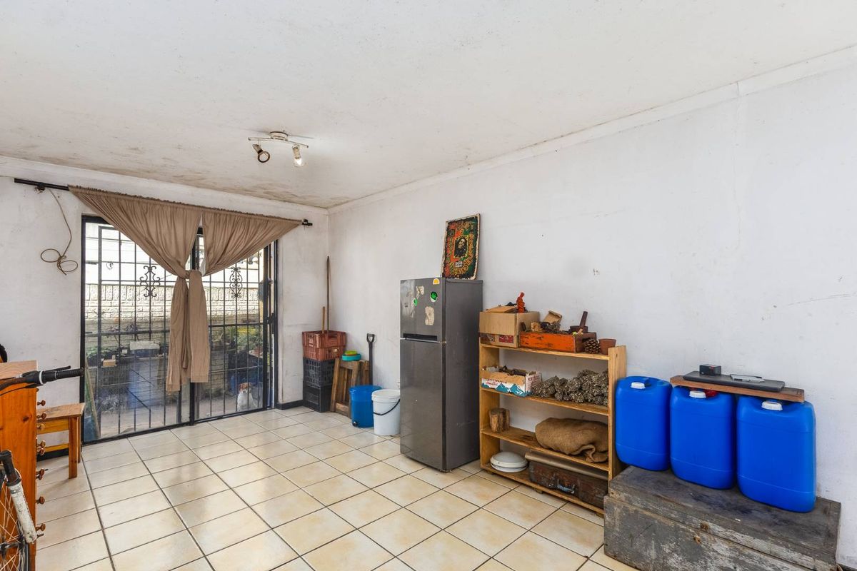 A living area featuring tiled flooring and a sliding glass door with security gate, showing signs of ceiling water damage and wall wear.